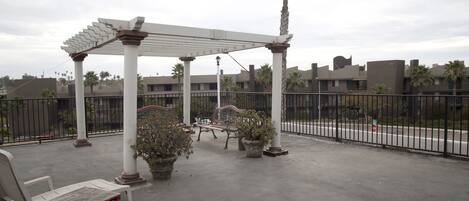A covered outdoor seating area with a pergola, benches, and potted plants.