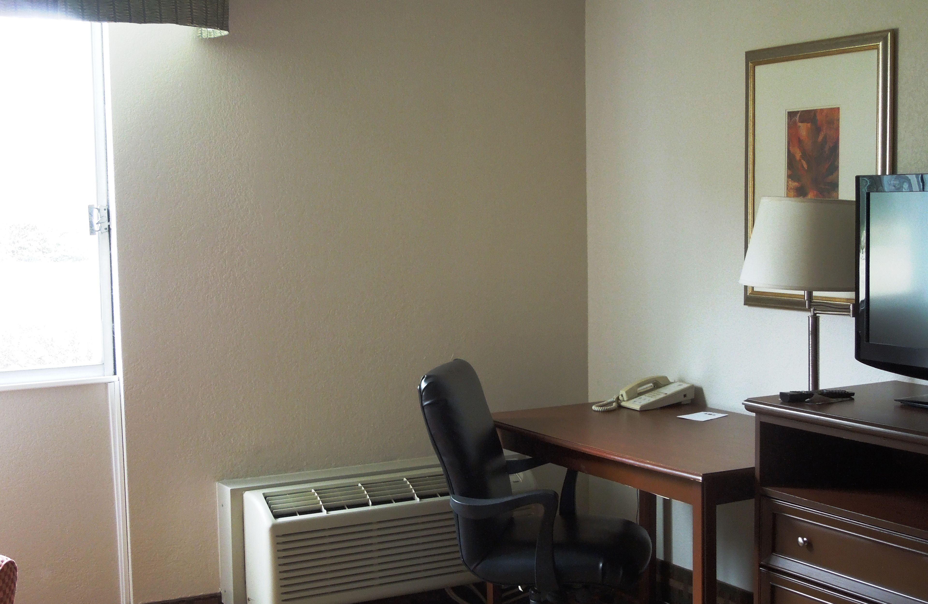 Una habitación de hotel con escritorio, silla, televisor, lámpara y radiador.