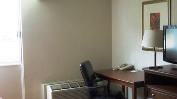 Una habitación de hotel con escritorio, silla, televisor, lámpara y radiador.