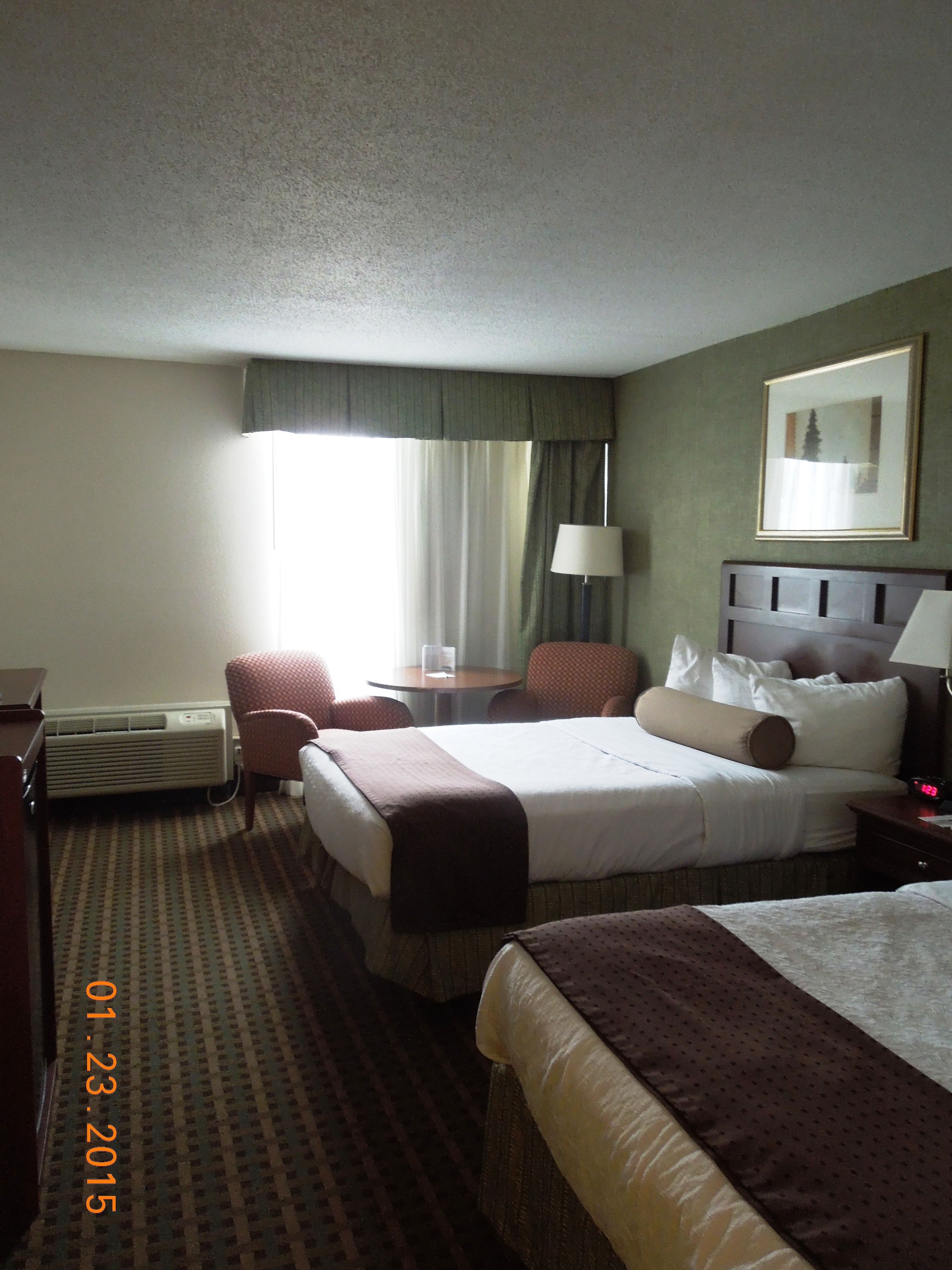 A hotel room with a large bed, two chairs, a desk, a lamp, and a heater.