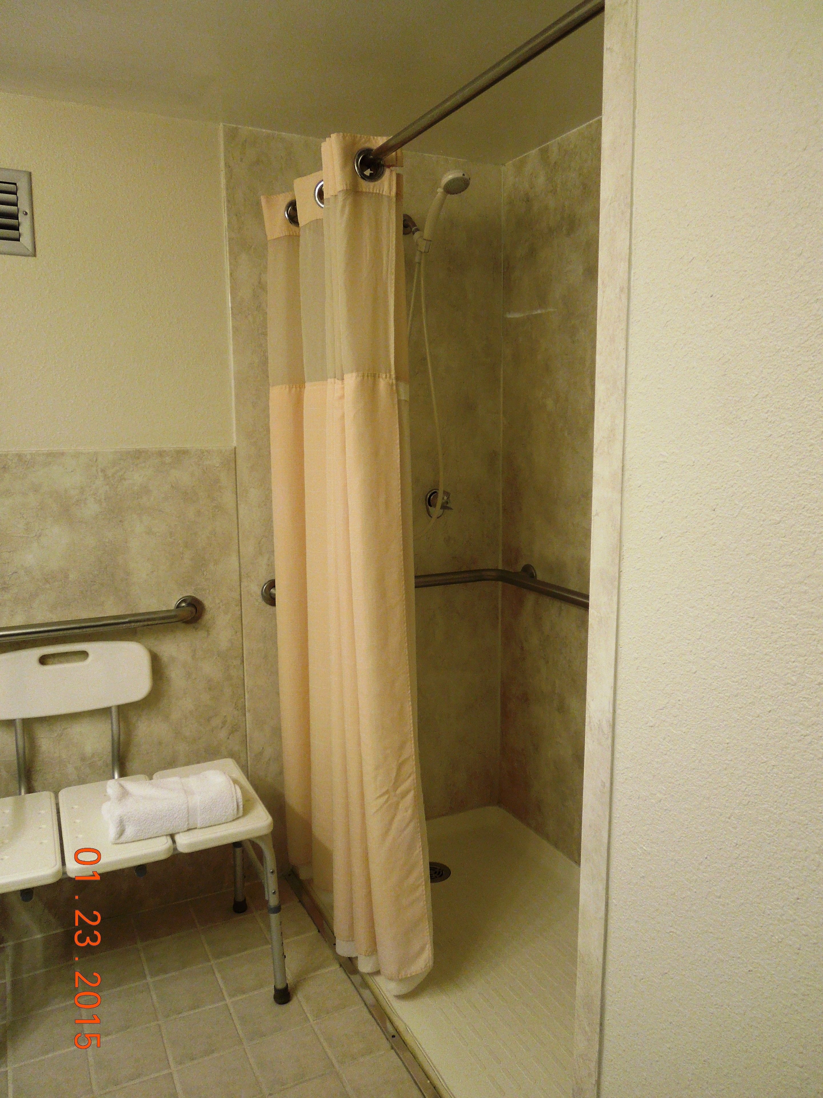 A shower stall with a beige curtain, a grab bar, and a bench with a towel.