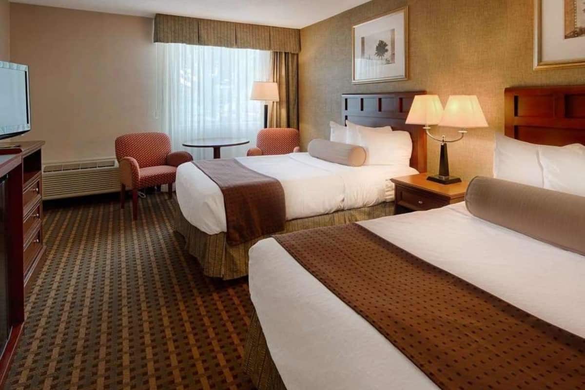 A hotel room with two beds, a desk, a chair, a TV, and a window with curtains.