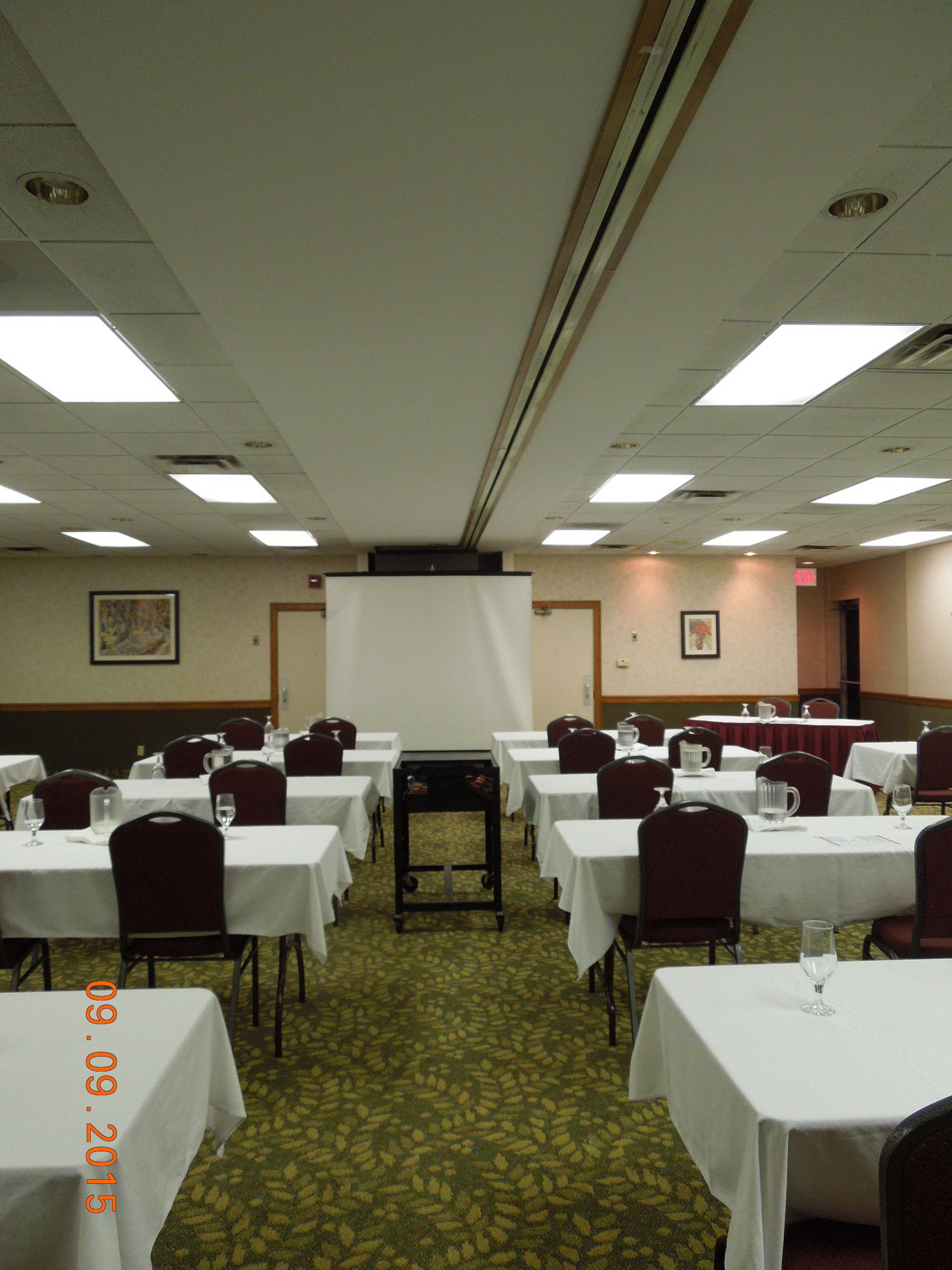 A conference room with multiple tables, chairs, and a projection screen.
