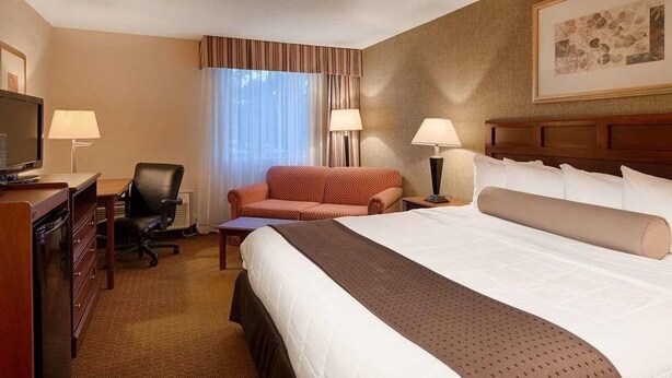 Quarto de hotel com uma cama grande, um sofá, uma mesa de escritório com um computador e uma televisão.