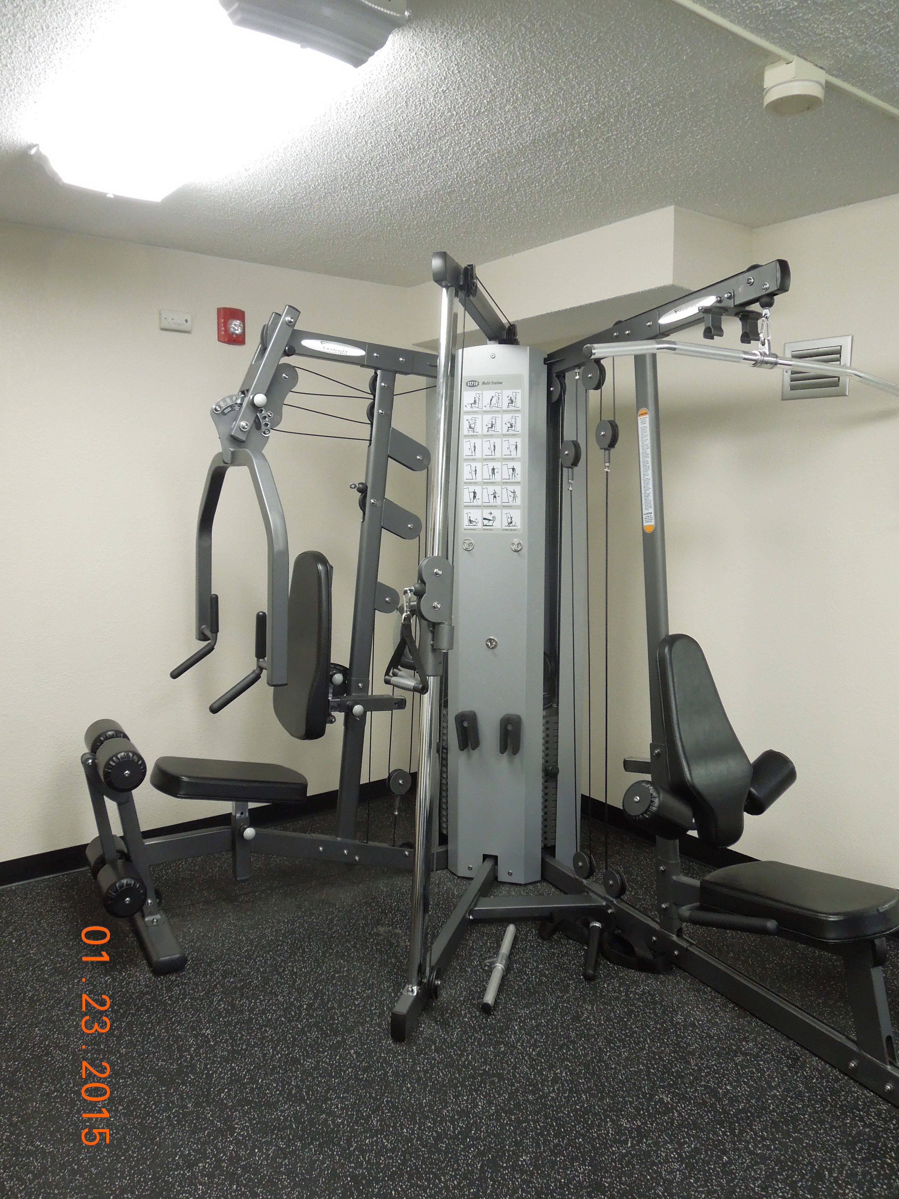 A gym with a multi-station workout machine, a bench, and a wall-mounted pull-up bar.