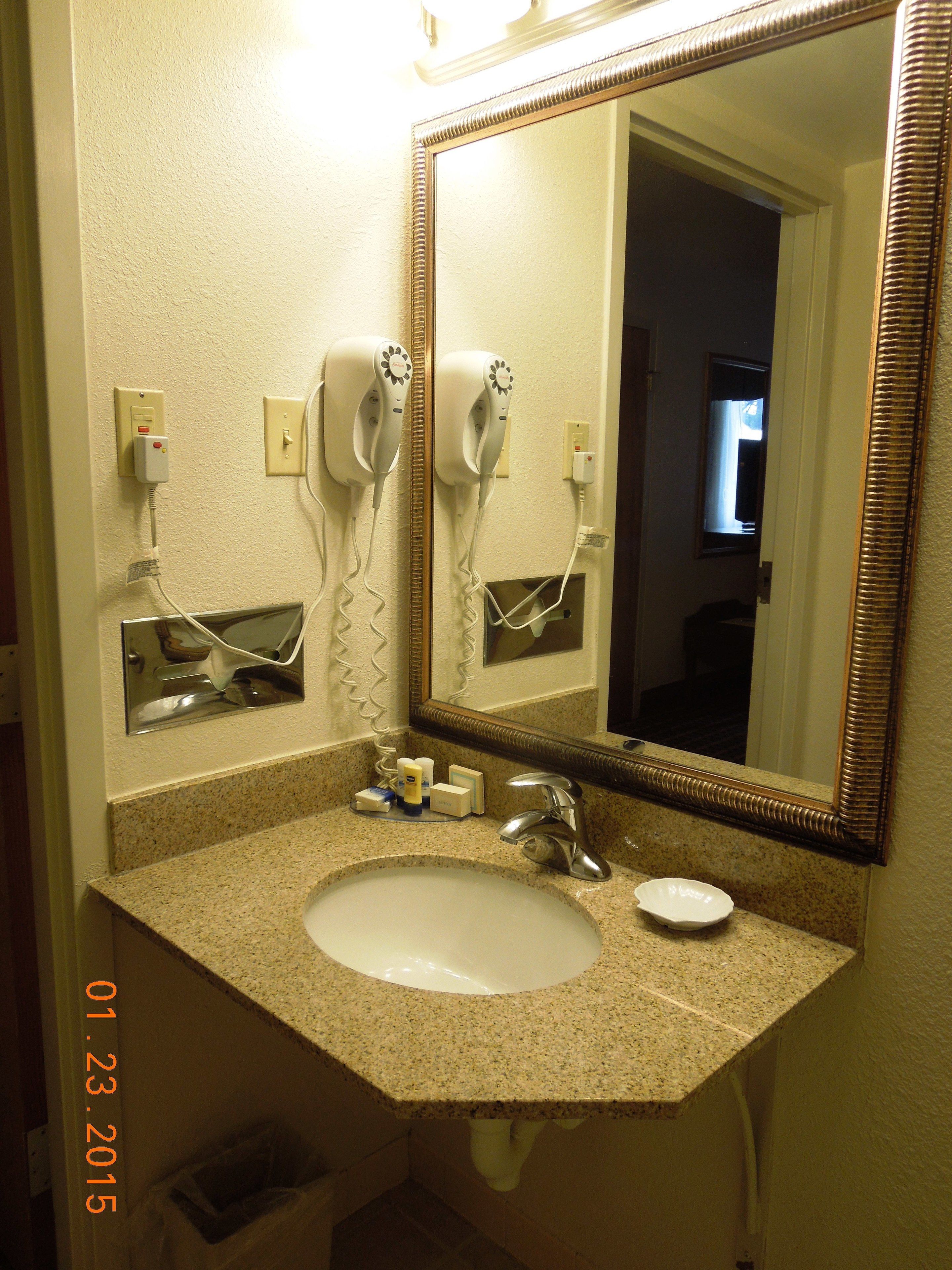 A bathroom with a granite countertop sink, a mirror, and two hair dryers mounted on the wall.