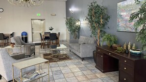 A modern waiting area with a chandelier, seating, a dining table, and a large plant. - Shilo Inn Suites - Salem (Salem)