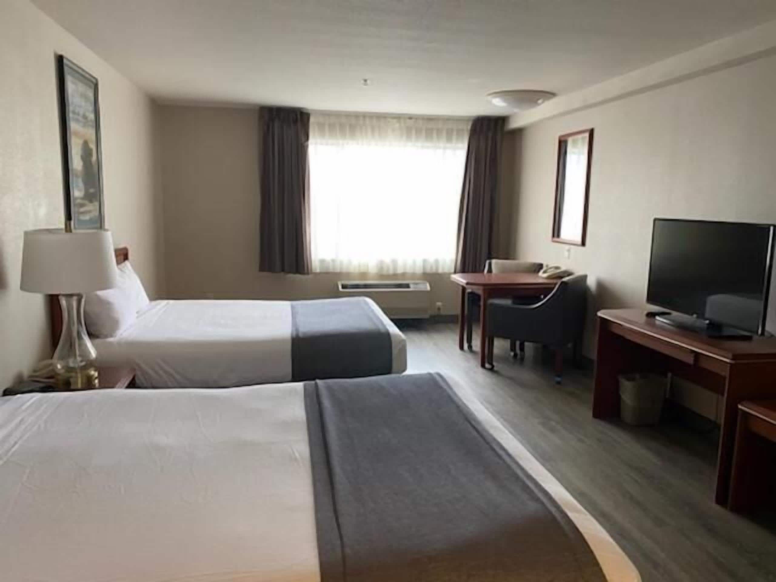 Habitación de hotel con dos camas, un escritorio, una silla, un televisor y una ventana con cortinas.