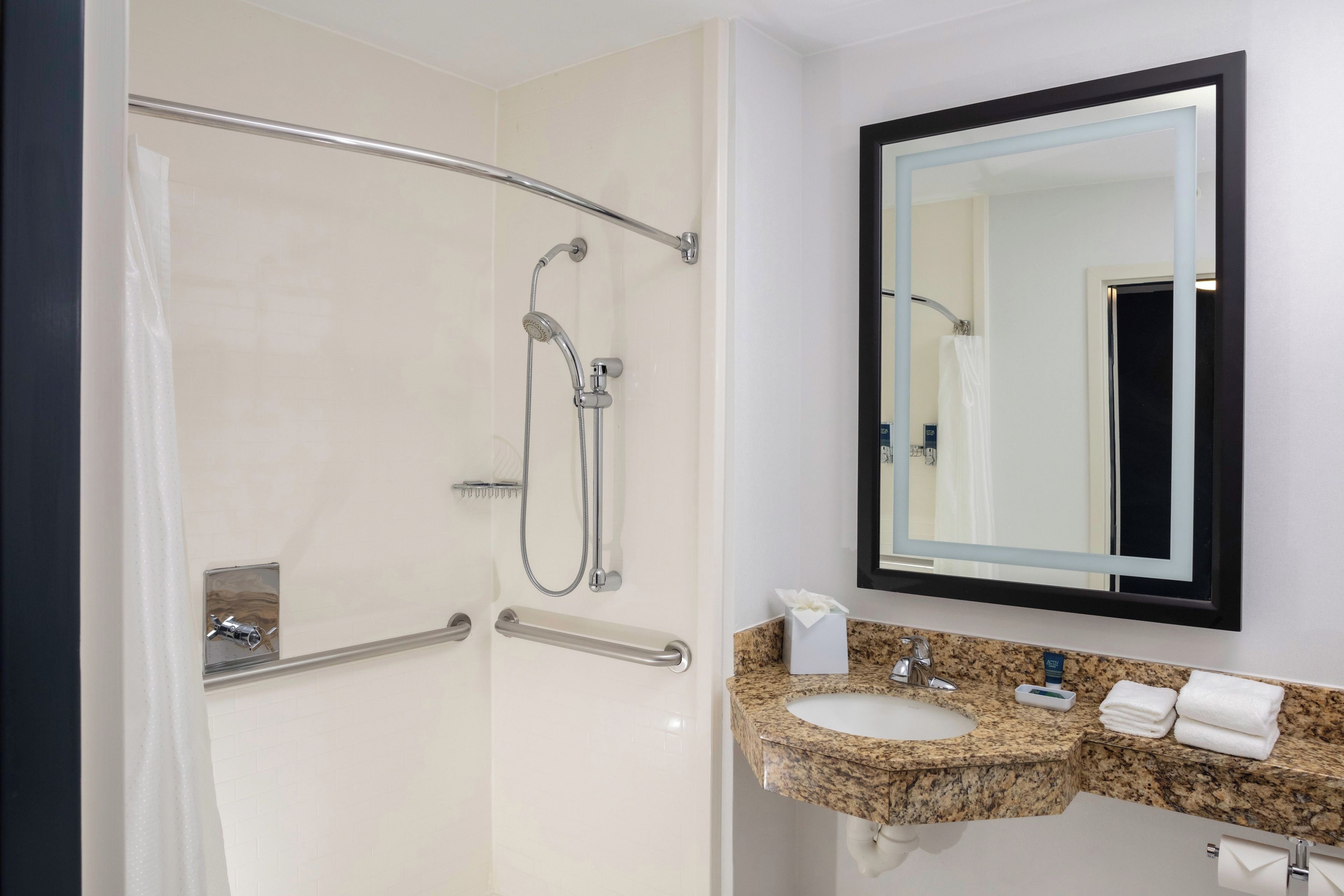 A bathroom with a walk-in shower, a sink with a granite countertop, a mirror, and a towel rack.