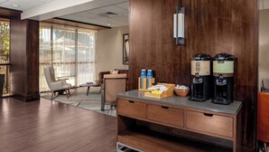 A hotel lobby with a wooden reception desk, coffee makers, and a seating area with a sofa and armchairs. - Four Points by Sheraton Memphis East (Memphis)