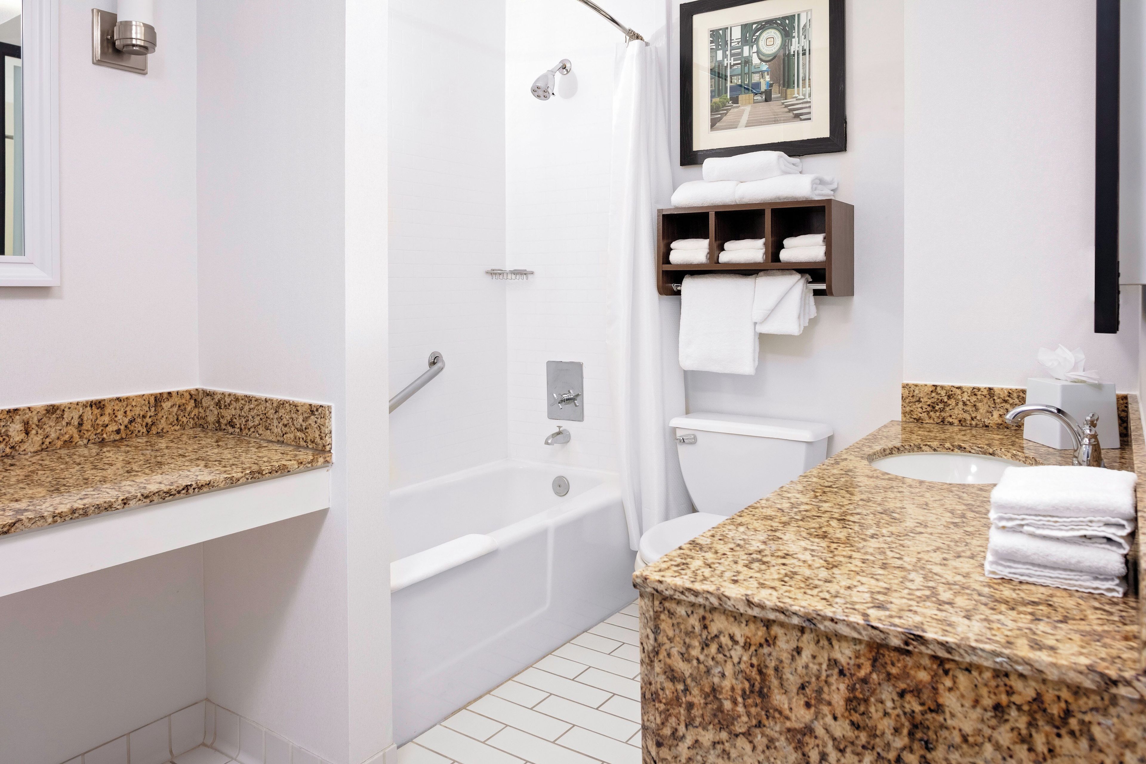 A modern bathroom with a granite countertop, a bathtub, a toilet, and a shower.