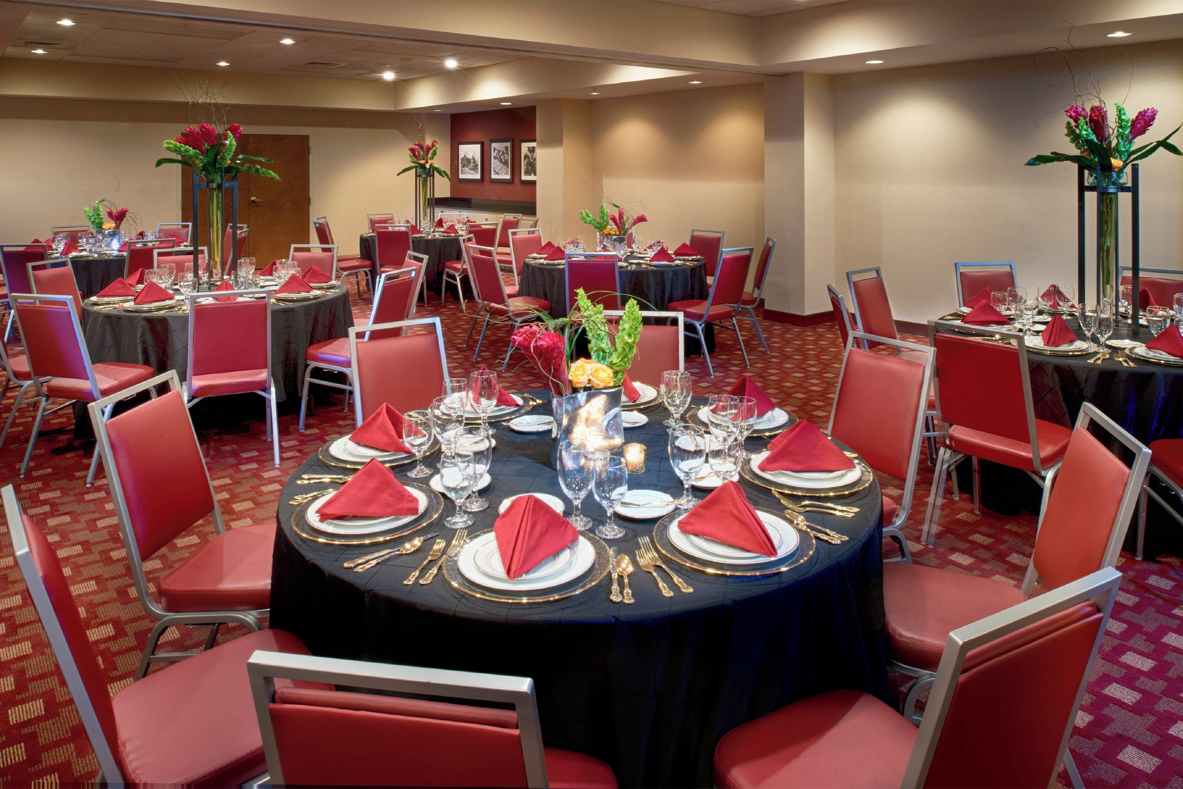 A banquet hall with round tables set for dining, red chairs, and floral centerpieces.