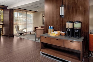 Un hall d’hôtel avec un comptoir d’accueil en bois, des machines à café et un espace détente comprenant un canapé et des fauteuils.