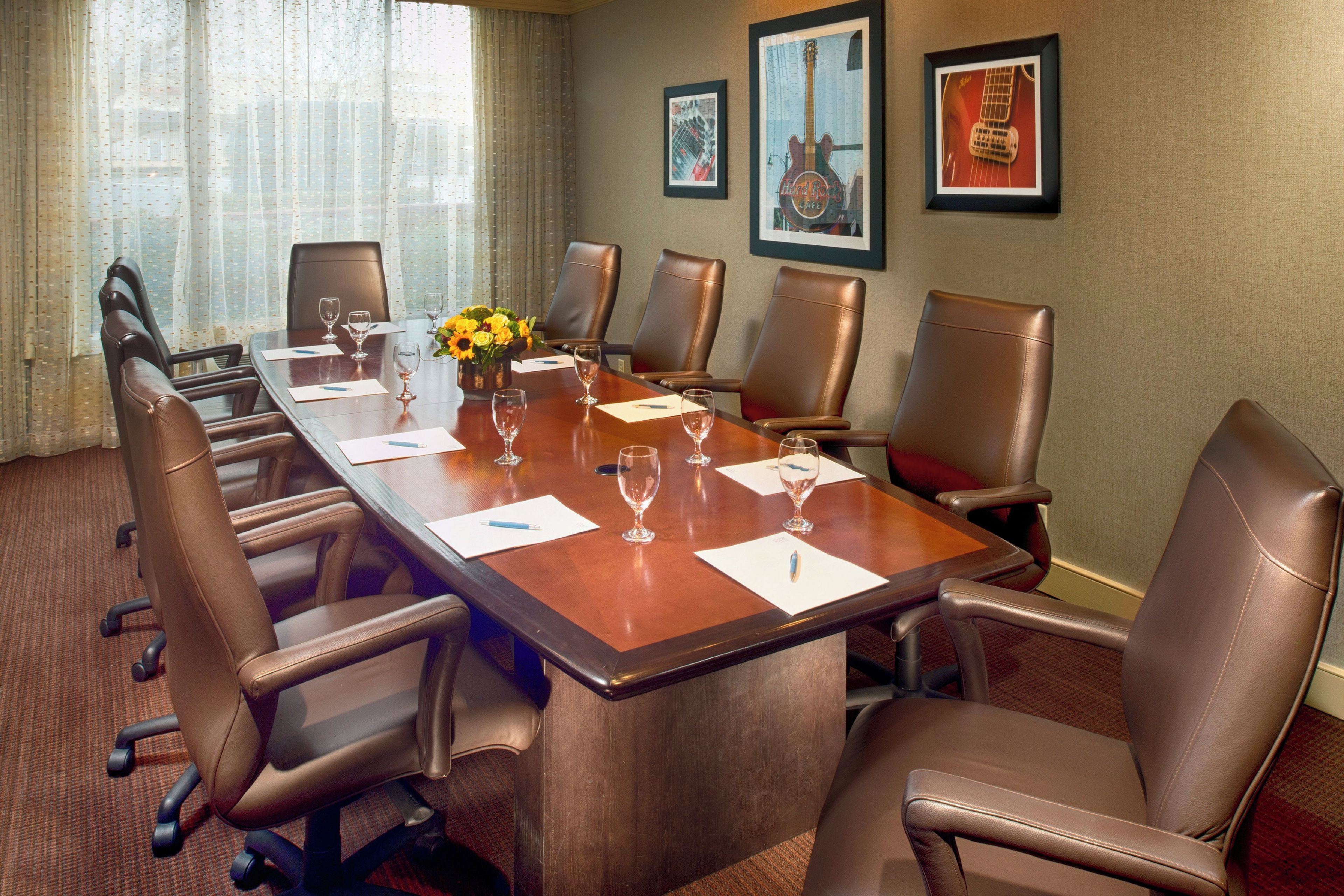 A conference room with a long table, six chairs, and a vase of yellow flowers.