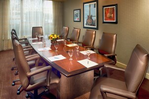 A conference room with a long table, six chairs, and a vase of yellow flowers.