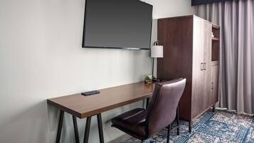 Habitación de hotel con escritorio, silla, televisor, armario y alfombra estampada.
