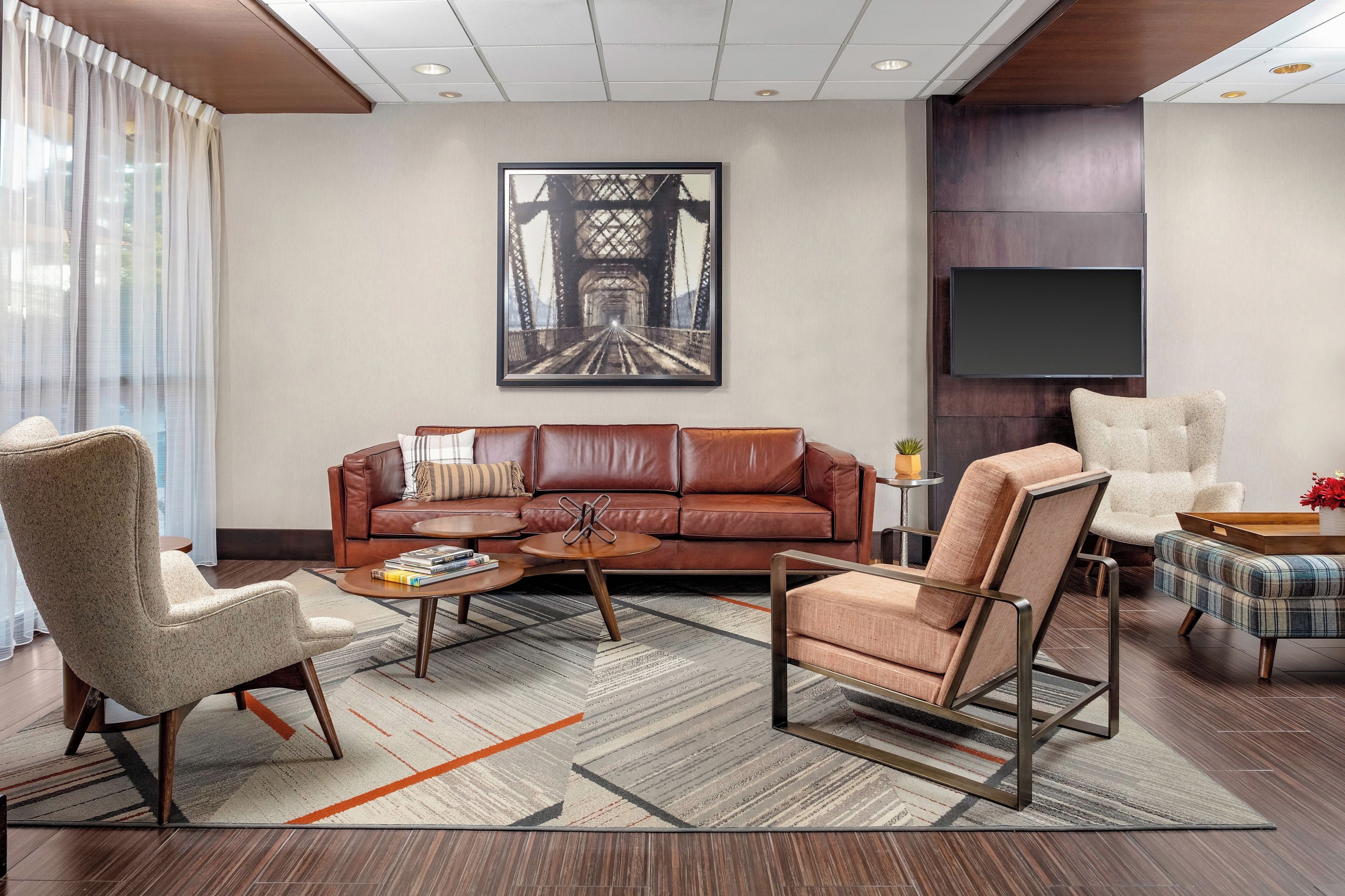 A modern living room with a leather sofa, a coffee table, and a large painting of a bridge.