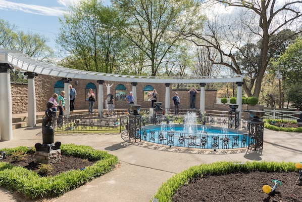 A courtyard with a central fountain, surrounded by a brick wall with arched windows, and a covered seating area.