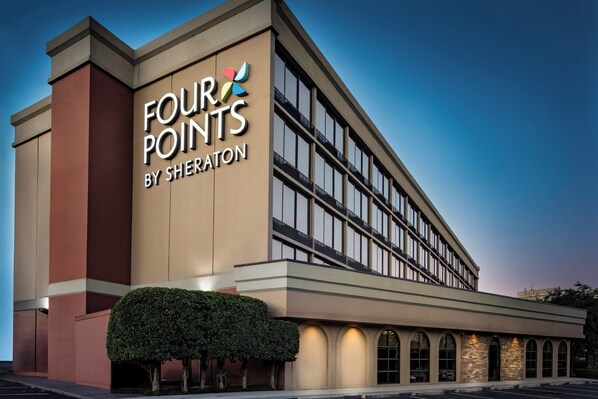 Un hotel llamado 'Four Points by Sheraton' con una fachada moderna, ventanas grandes y una entrada bien iluminada.