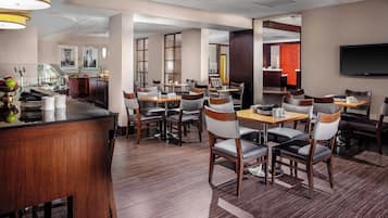 A hotel dining area with multiple tables and chairs, a bar, and a reception desk.