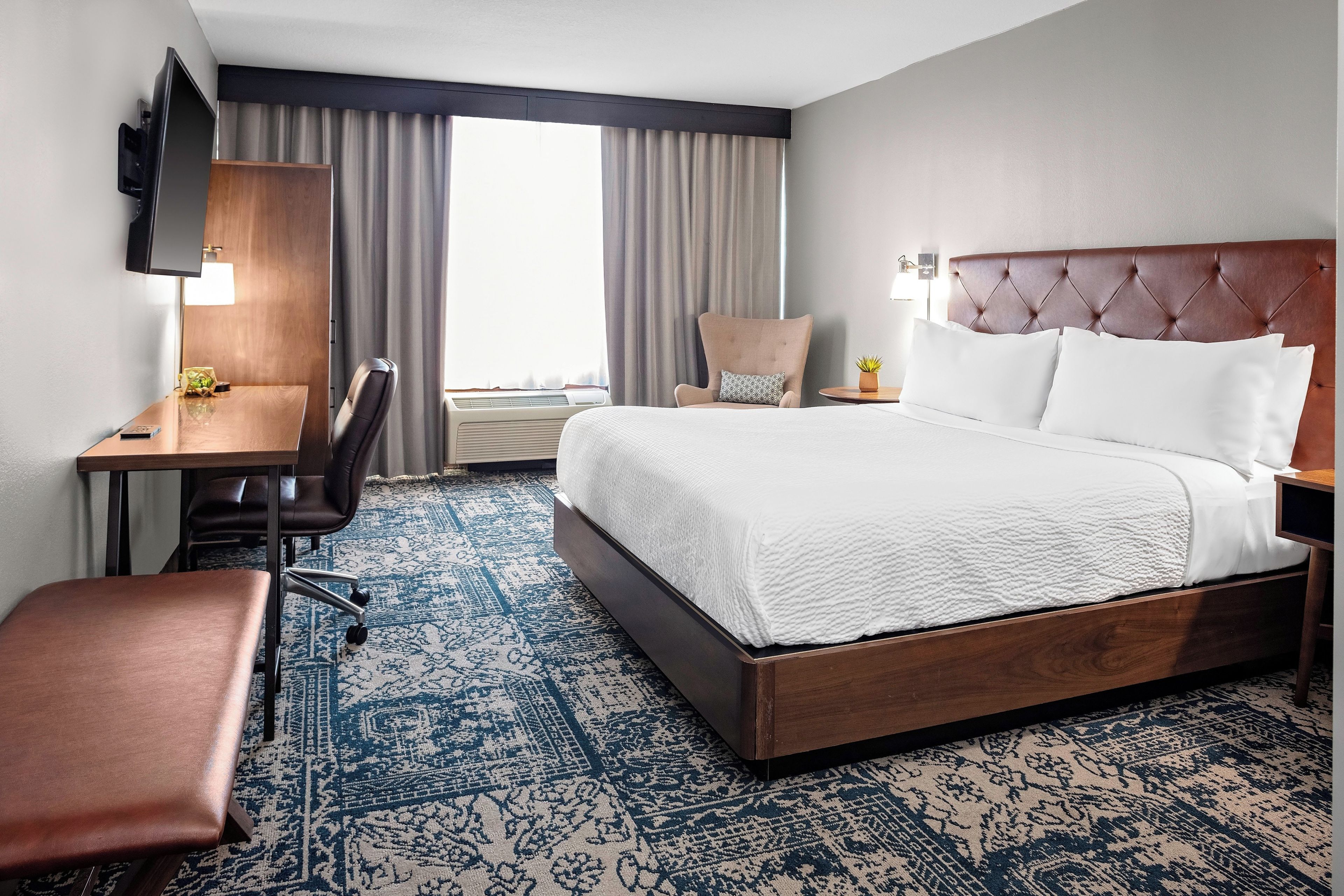 A hotel room with a bed, a desk, a chair, a television, and a window with curtains.