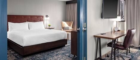 A hotel room with a large bed, a desk with a chair, a television, and a small table with a lamp.