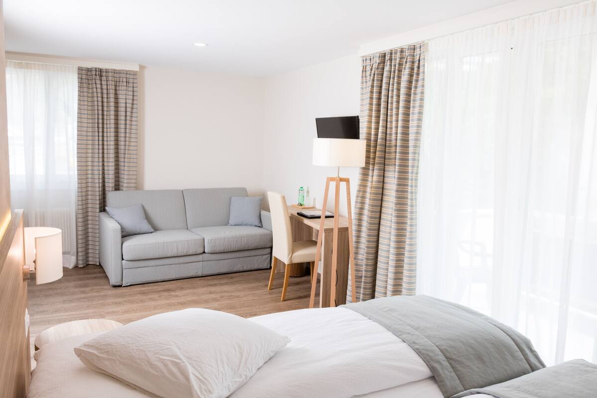 A modern hotel room with a bed, a sofa, a desk, and a chair.