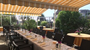 An outdoor dining area with tables set for a meal, surrounded by greenery and under a striped awning. - Hotel de Chailly (Montreux)
