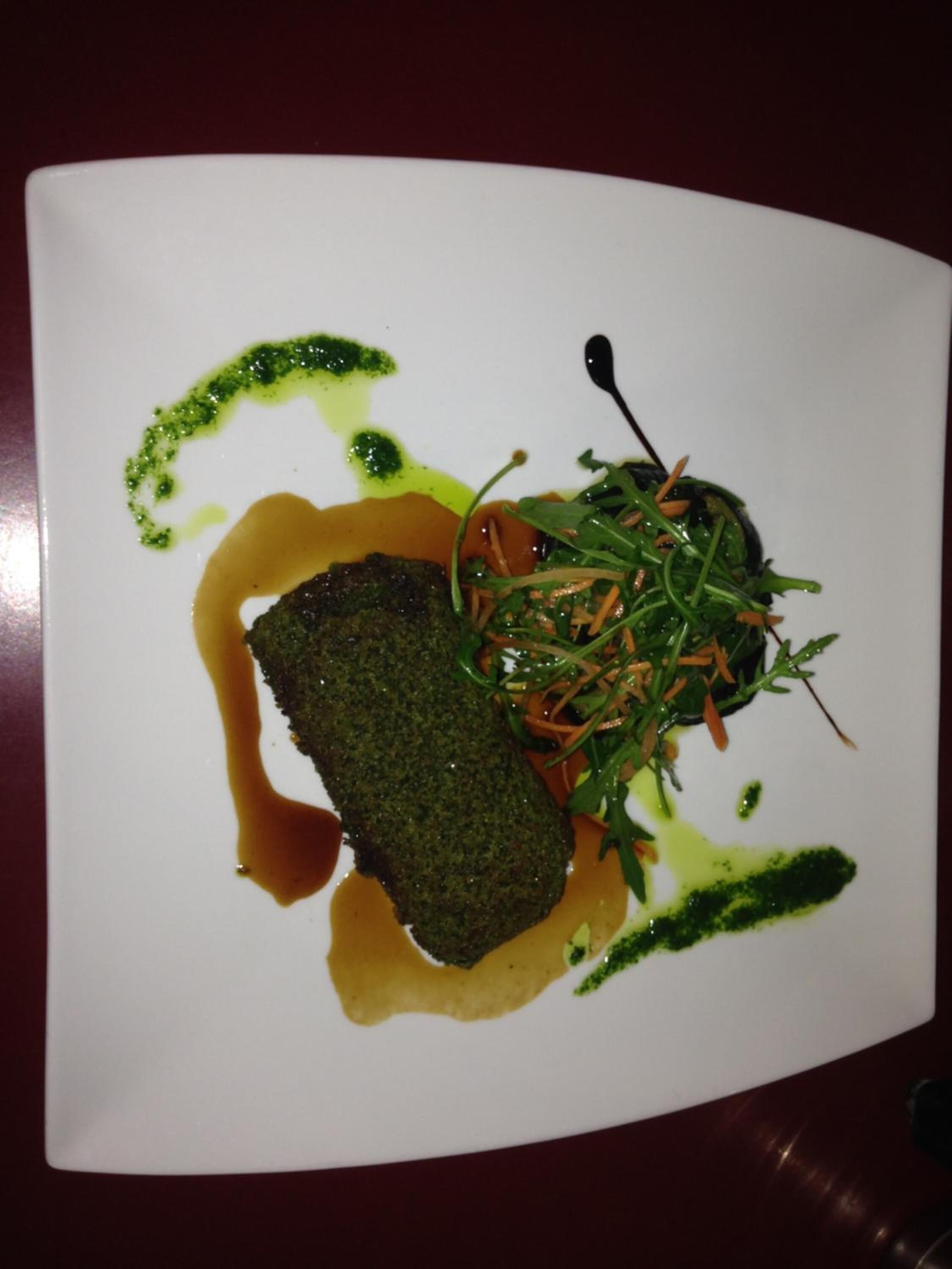 Une assiette carrée contenant un légume vert foncé, peut-être une betterave, et une salade verte avec des feuilles et de fines tranches de carottes. On y trouve deux sauces vertes, l’une avec un motif en fines lignes et l’autre avec un motif en points.