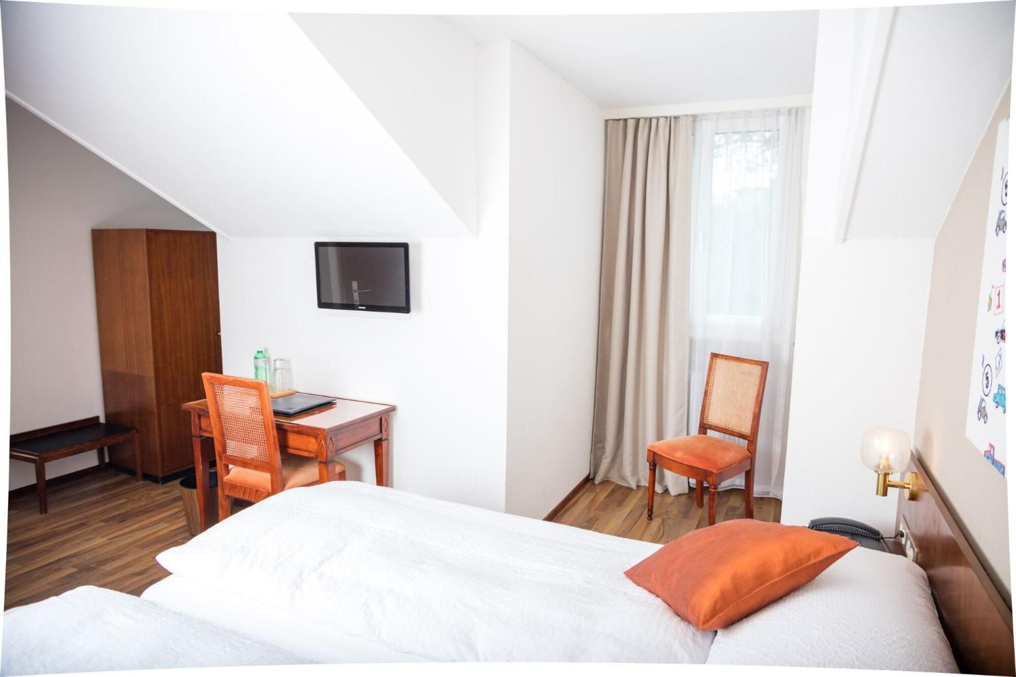 A hotel room with a bed, a desk with a chair, a television, and a window with curtains.