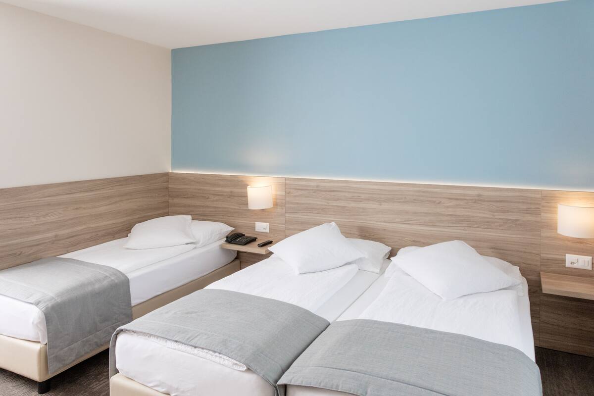 A hotel room with two single beds, a wooden headboard, bedside lamps, and a light switch on the wall.