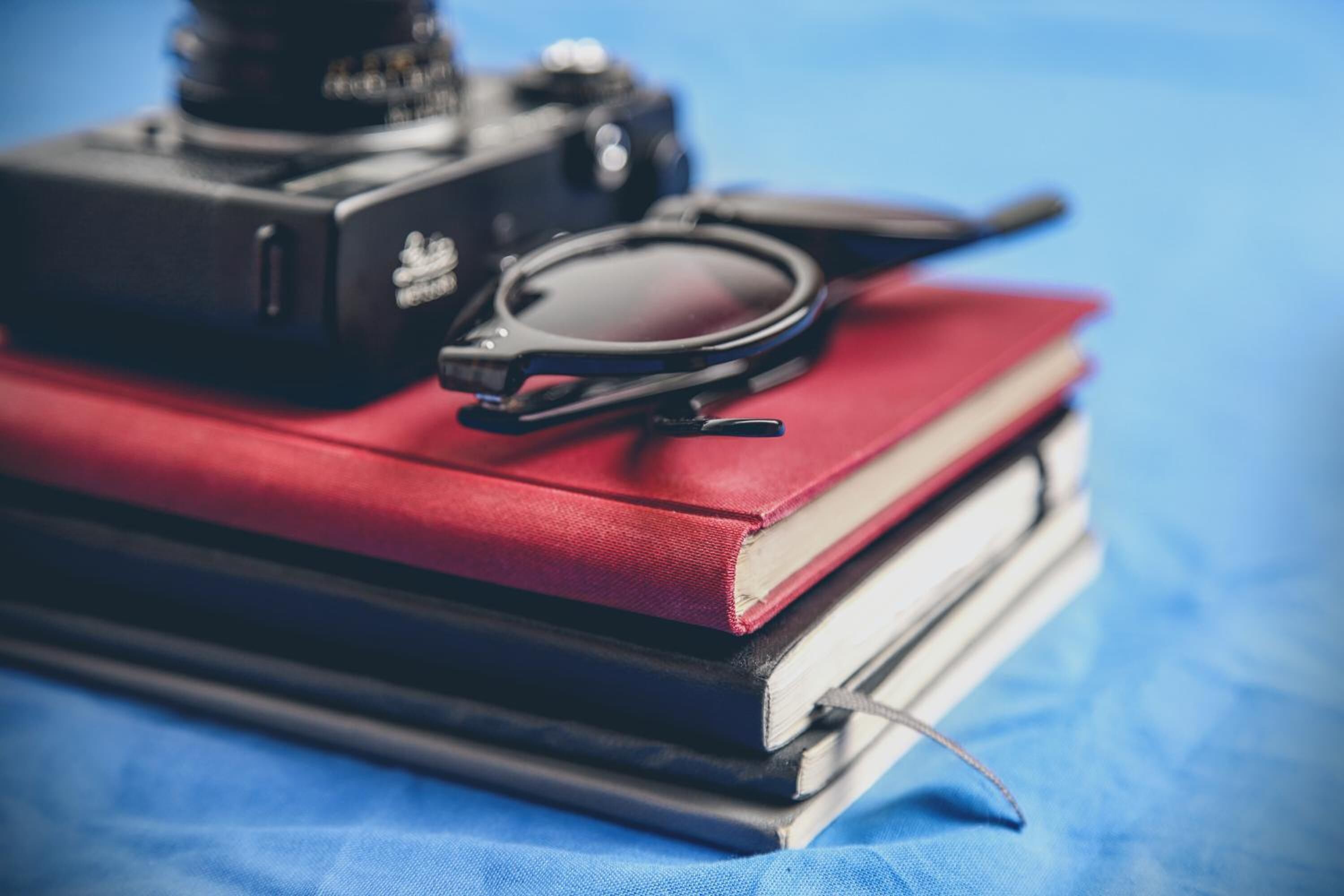 A camera, a magnifying glass, and a stack of books on a blue fabric surface.