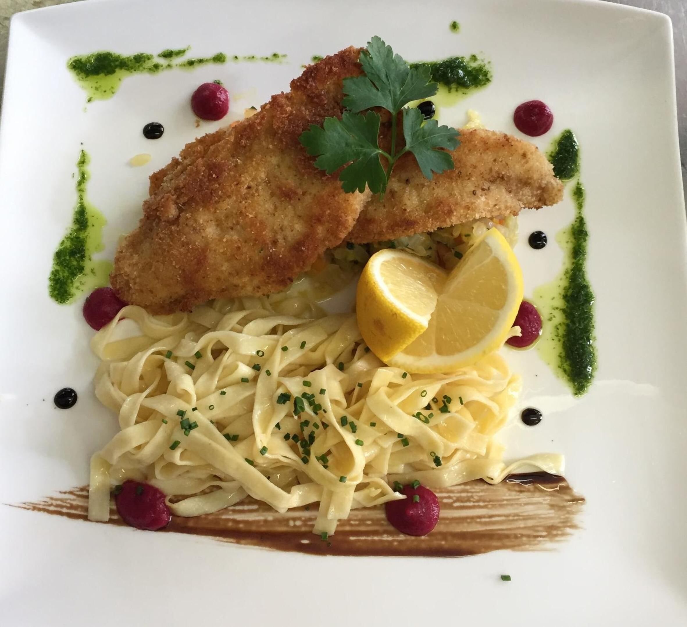 En upplagd rätt med panerade fiskfiléer, pasta, citron och garnering.