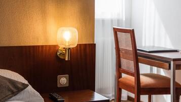 Quarto de hotel com cabeceira de madeira, mesa de cabeceira com abajur, controle remoto e uma cadeira.