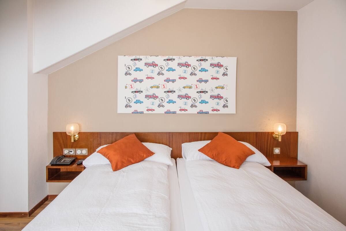 A hotel room with two beds, a ceiling with a sloped design, and a wall with a patterned artwork.