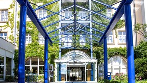 Entrada de un edificio con fachada de vidrio y elementos estructurales azules.
