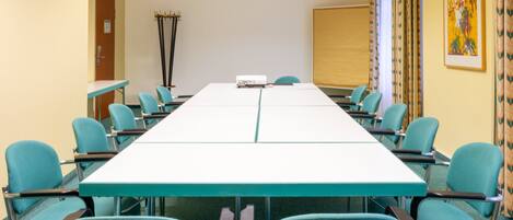A conference room with a long table, teal chairs, a projector, and a whiteboard.