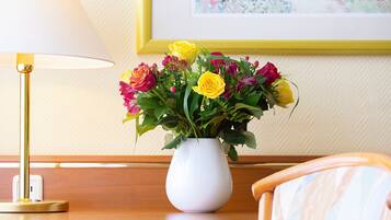 A white vase with a bouquet of flowers on a wooden table, a lamp, and a framed picture on the wall.