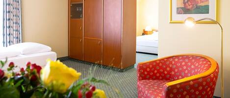 A hotel room with a bed, a wardrobe, a red armchair, and a painting on the wall.