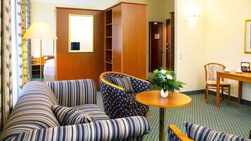 Een hotelkamer met een gestreept zithoek, een ronde houten tafel met een vaas, een eettafel met stoelen en een garderobe.