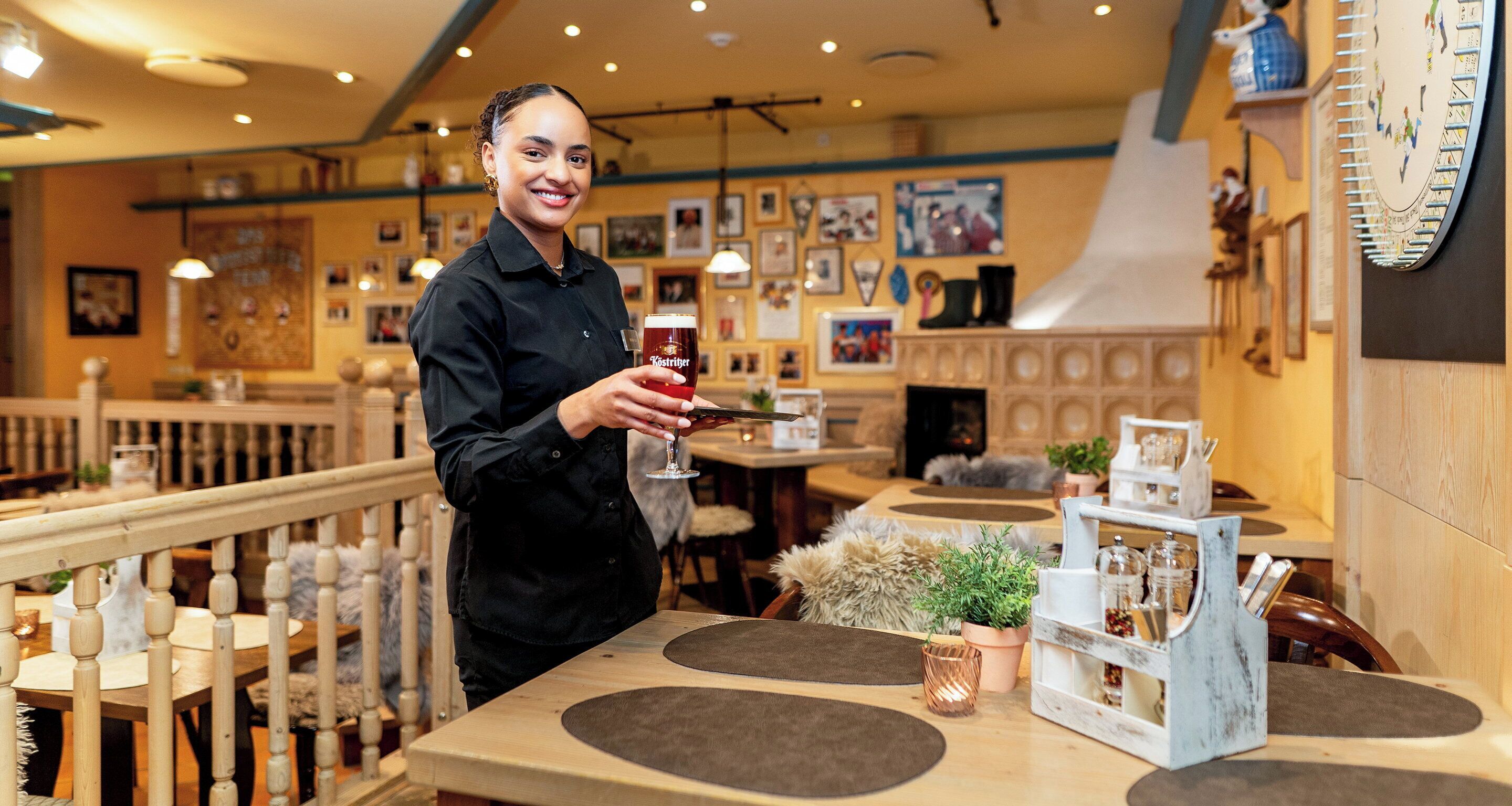 Une personne tenant un verre de bière dans un restaurant dont le mobilier est en bois et qui est décoré d’une horloge murale.