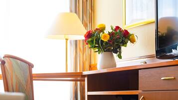 A wooden desk with a vase of flowers, a lamp, and a television.