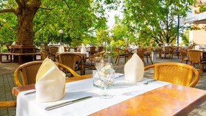 Un área de comedor al aire libre con sillas y mesas de mimbre, rodeada de árboles.