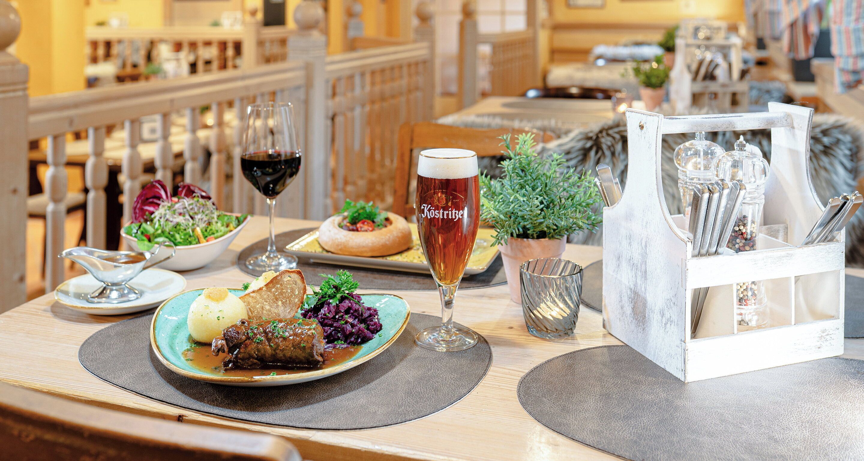 A dining table with a plate of food, a glass of beer, and a menu holder.
