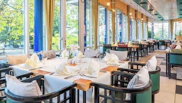 Un restaurante con mesas dispuestas para comer, ventanas amplias y vistas al exterior.