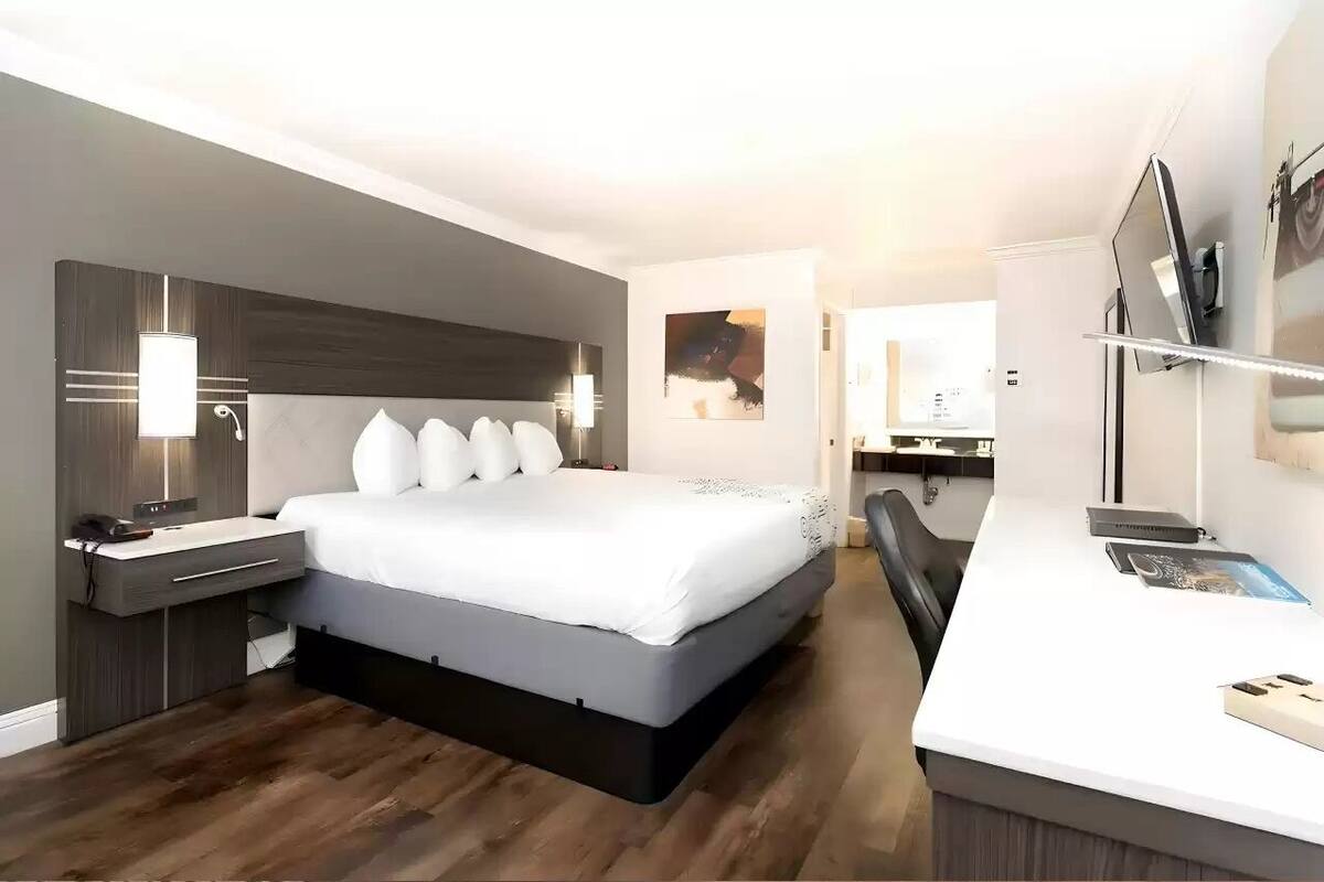 A modern hotel room with a bed, bedside table, desk, chair, and a mirror.