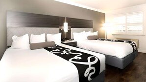 A hotel room with two beds, a modern headboard, bedside lamps, and a large window with blinds.