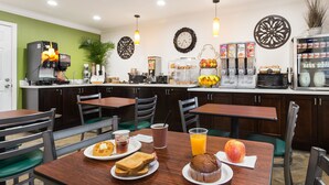 A breakfast area with tables, chairs, a coffee machine, and a fruit display.