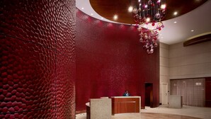 Un hall d’entrée avec un mur rouge à texture, un comptoir d’accueil et un lustre.
