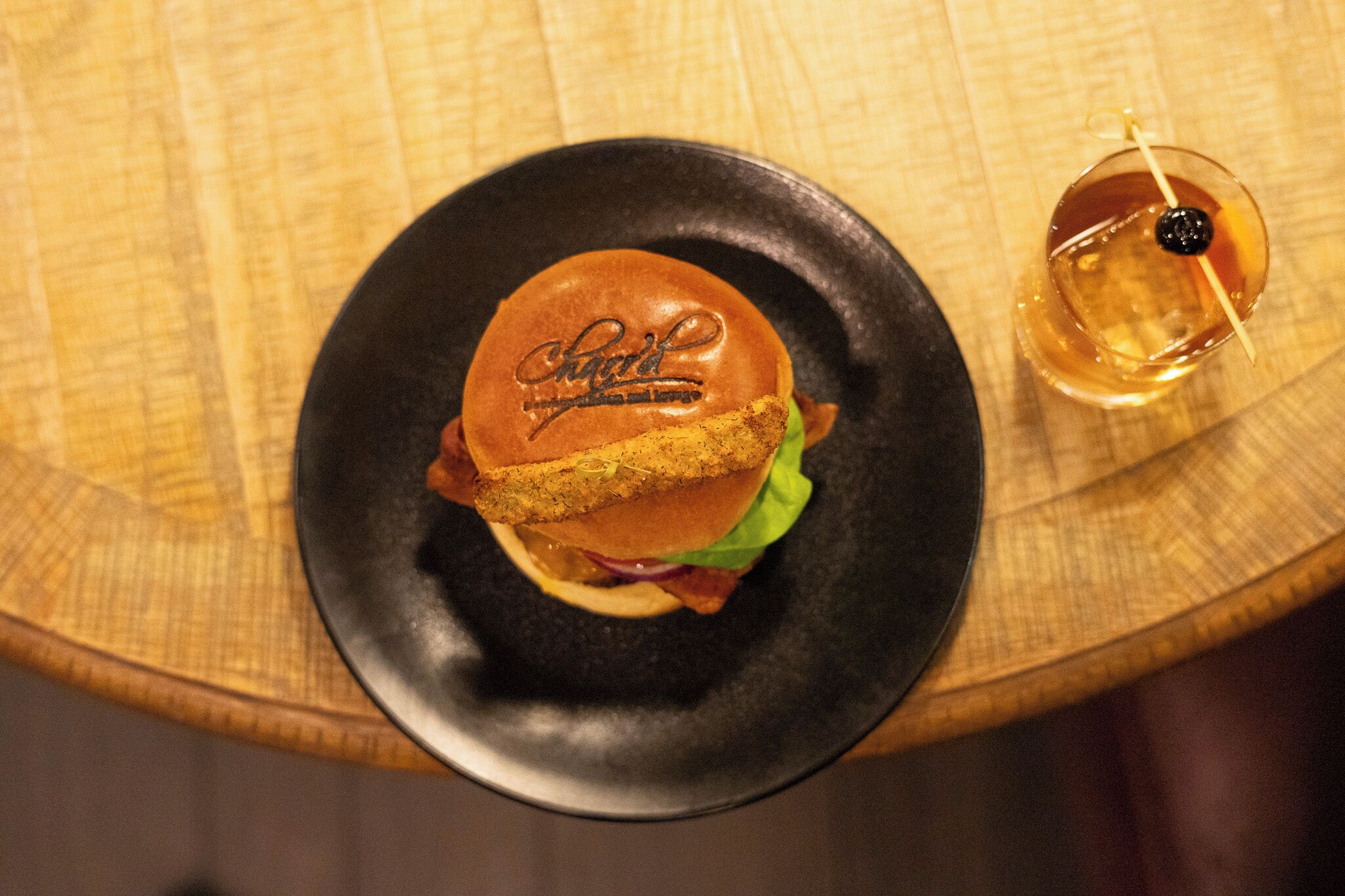 Un sandwich sur une assiette noire, avec une boisson à côté.